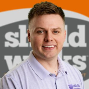 man with purple polo and shieldworks logo background