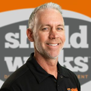 Josh Final man with black polo shirt and shieldworks logo background